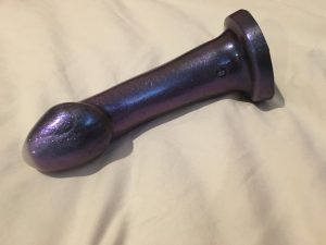 A picture of a purple sparkly g-spot dildo with a white tip on white bedsheets