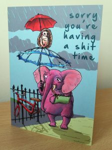 Card with a picture f an elephant and a hedgehog holding umbrellas on it that says 'sorry you're having a shit time'