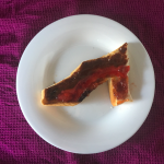 Picture of a piece of toast in the shape of a shoe with jam and marmite on top in a pattern