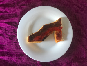 Picture of a piece of toast in the shape of a shoe with marmite and jam on top in a pattern