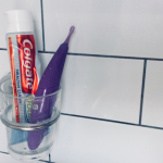 Colgate toothpaste in toothbrush cup stuck to tiled wall, slim purple Zumio sex toy in the cup beside it