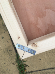 Corner detail of wooden frame with screws and a silver metal strip holding them together