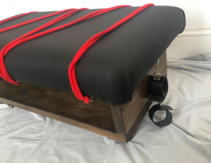 Corner view of spanking bench, with ropes and handcuffs attached to the mount points