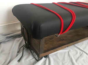 Corner view of spanking bench showing red and green ropes attached to mount points
