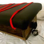 Picture of a soft thick pleather top covering an otherwise normal-looking coffee table. Ropes and handcuffs are tied to mounting points underneath the table top