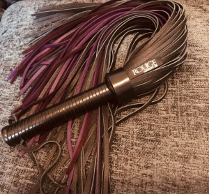 Picture of a black and purple leather flogger with the brand name 'rouge garments' visible