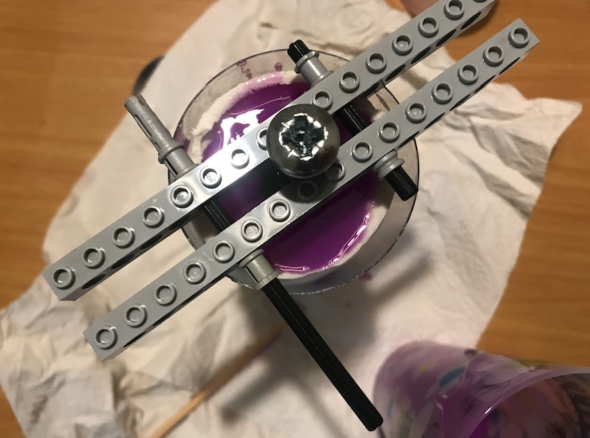 Lego contraption balanced on a plastic tube which is filled with purple silicone
