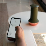 Hand holding phone with MyHixel premature ejaculation app open on it, with device sitting on table nearby