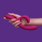 We-Vibe Nova 2 - dark pink silicone rabbit vibrator, held in hand on a purple background