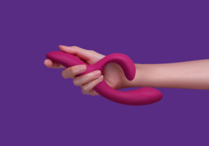 We-Vibe Nova 2 - dark pink silicone rabbit vibrator, held in hand on a purple background