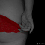 A woman tugs at her red knickers, just about to pull them down