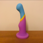 Slim dildo with wide pink base, shot of yellow silicone in the middle, then blue at the slim, curved tip