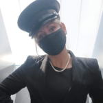 Image of a woman in a chauffer's cap, black jacket and black face mask