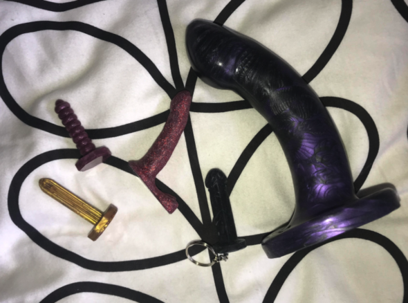 Image of a large Godemiche Morpheus sitting next to four tiny miniature dildos of varying shapes and colours
