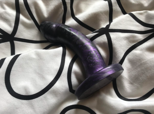Godemiche Morpheus - black and purple curved dildo - lying on a bed