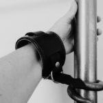 Hand in a leather wrist cuff, attached to and gripping a bedpost