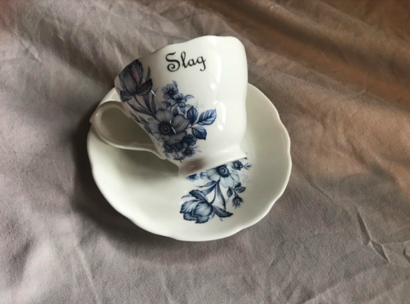 Delicate ceramic teacup and saucer with blue floral design, and in fancy writing on the cup it says 'slag'