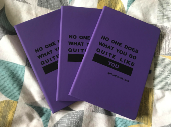 Three purple notebooks displayed on a bedspread. On the front of them there's the slogan 'no one does what you do quite like you' and GOTN's url.