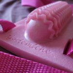 Image of a pink silicone pad with a raised lump in the middle covered in textured waves, and a pink strap attached to the sides