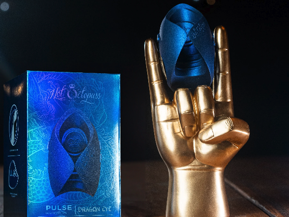 Image of a very shiny irridescent blue PULSE box, with the toy (a blue helmet-looking object) perched betwixt the forefinger and pinkie finger of a fake gold hand