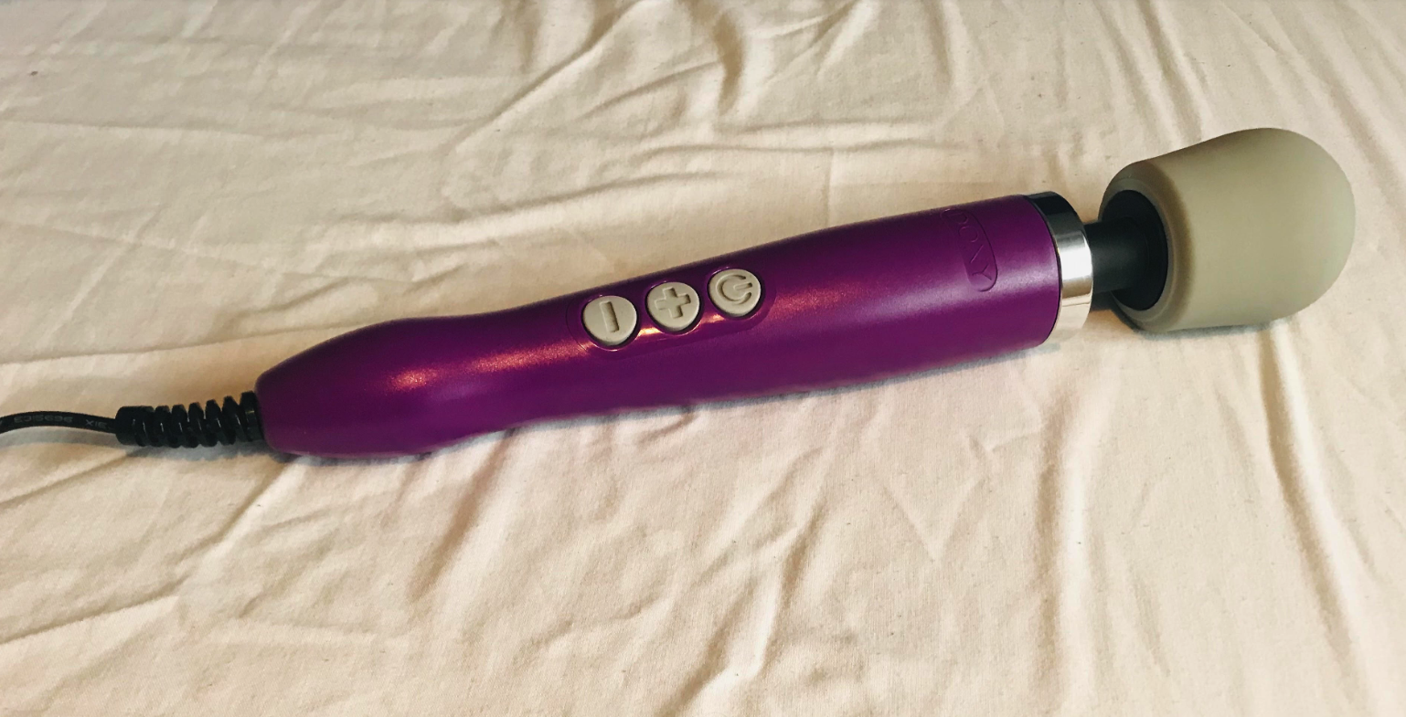 Image of a purple Doxy wand with grey head against white sheets in background