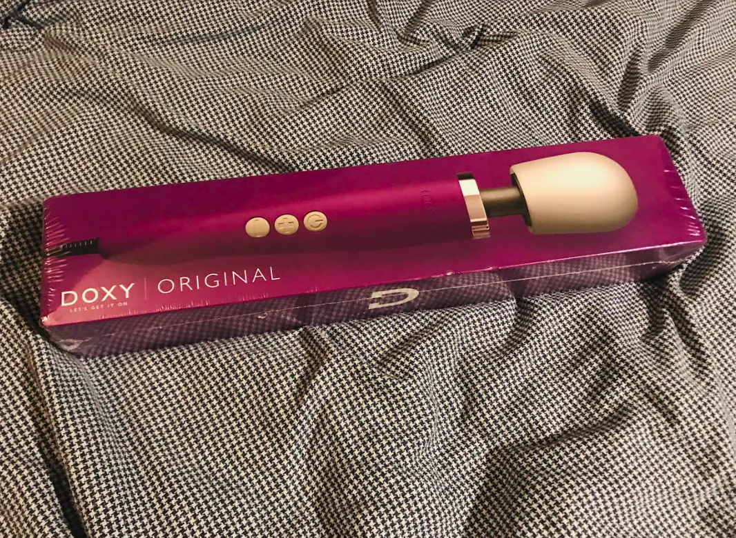 Image of a Doxy wand vibrator with purple body in purple box against blue duvet cover
