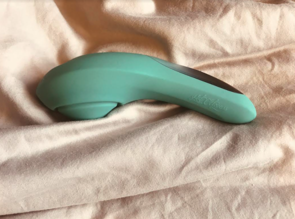 Image of a green sex toy with wider end that has a circular plate with a tapered 'tip' and a narrower handle, with gold buttons in the shape of a plus, minus and circle symbol