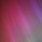 Image of a pink/purple/green aurora in the sky, with a few stars