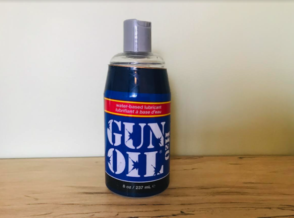 Bottle with click-to-open spout full of clear liquid, with blue label that says 'gun oil' in very military style font. It is stylistically very aggressive, and looks like you might use it too oil an actual gun. 