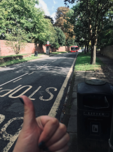 Image of a bus stop on a sunny/shady street, GOTN's thumb in foreground and single decker bus in background