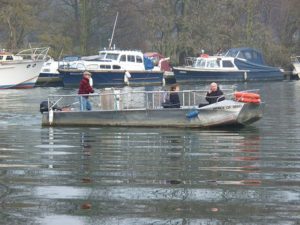 A small white boat with three people and some life rings on it, travelling across the river