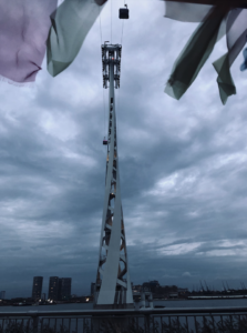 Shot of the tower that holds the cable car, with a couple of pods on the wires, and cloudy sky in the background