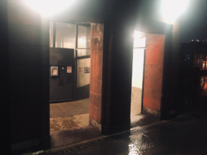 Dark building with light shining out of two doorways leading to an industrial looking lift