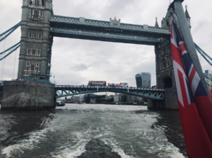 Shot from the river beneath Tower bridge, bridge in background with red bs going over it and water wake in foreground