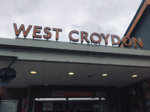 Shot of the orange letter sign that welcomes you to west croydon station, grey sky in background