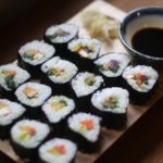 Wooden platter with a selection of vegan sushi rolls, and side bowl of soy sauce for dipping
