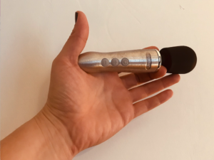 Hand holding a tiny version of a Doxy wand massager - metal body with bulbous black silicone head, about palm size