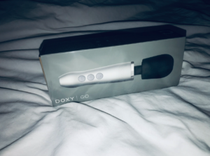 Grey box with small silver-bodied, black-headed wand toy on the front, on background of white sheets