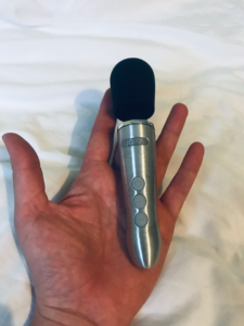 Doxy go (wand-shaped sex toy with a silver brushed metal body and black silicone head) nestling in the palm of GOTN's hand