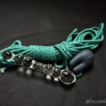 On a black sheet, a display of sex toys: bbeautiful teal-coloured rope, a knobbly glass dildo and a small black bunny-eared clit vibe